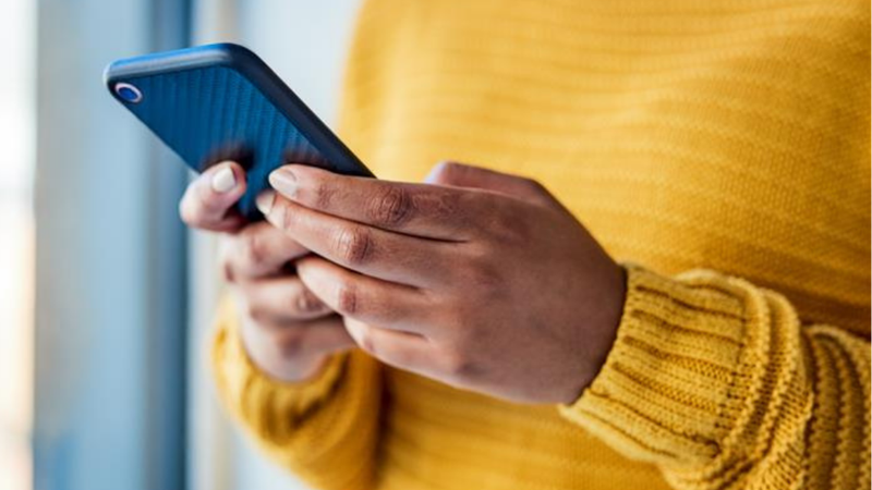 A close up photograph of a person in a yellow jumper holding a phone in their hands.