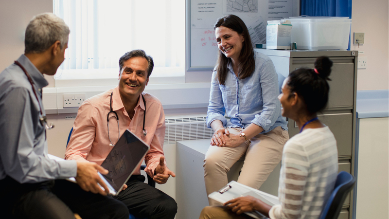 Group of clinicians sat in an office having a meeting and smiling
