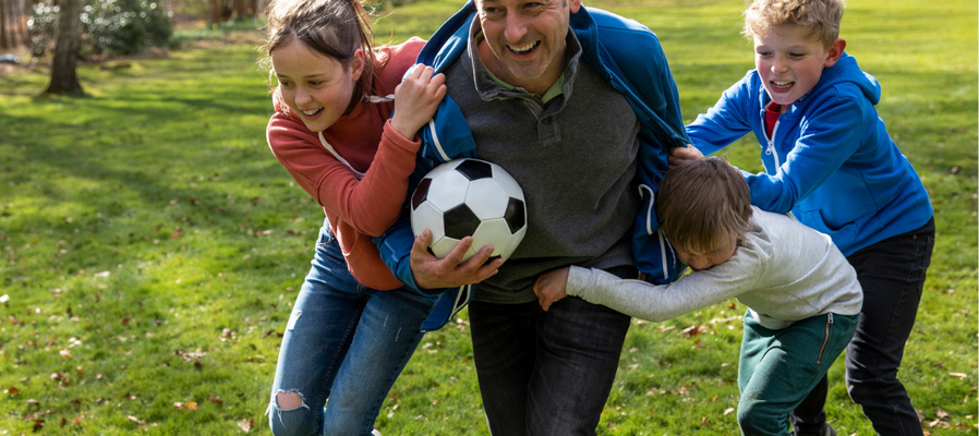 Image of a father playing football with three young children