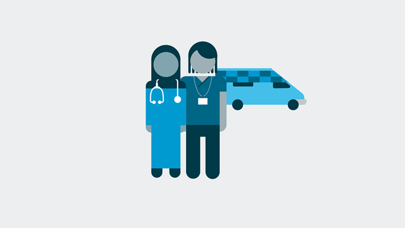 Two health and care workers standing together with an ambulance in the background.