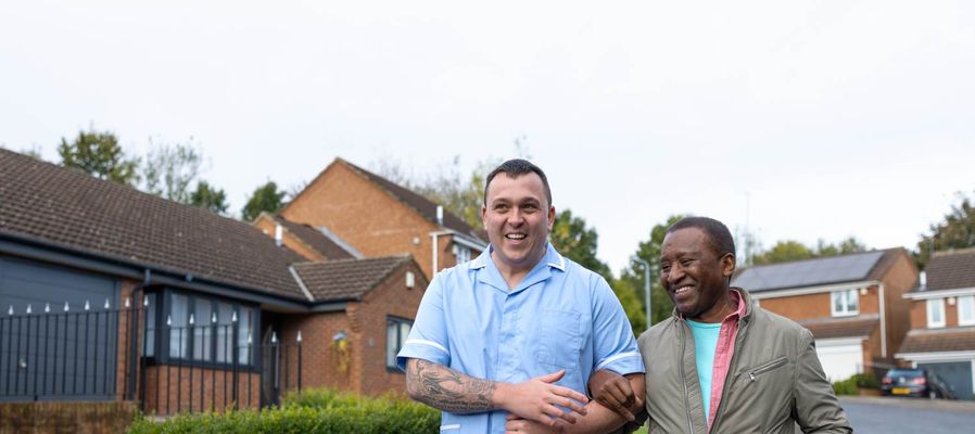 A health care professional and patient smile and walk along a quiet street.