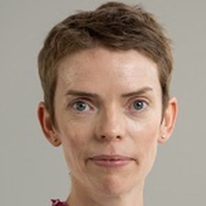 Portrait of a person with short hair, wearing a white and pink patterned shirt, against a plain background.