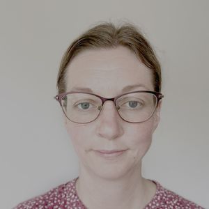 Person wearing glasses and a red polka dot top, looking at the camera with a neutral expression against a plain background.