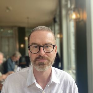 A man with glasses and a beard in a white shirt.