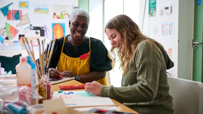 Two people enjoying an art activity at a table, surrounded by colorful supplies and paintings on the wall.