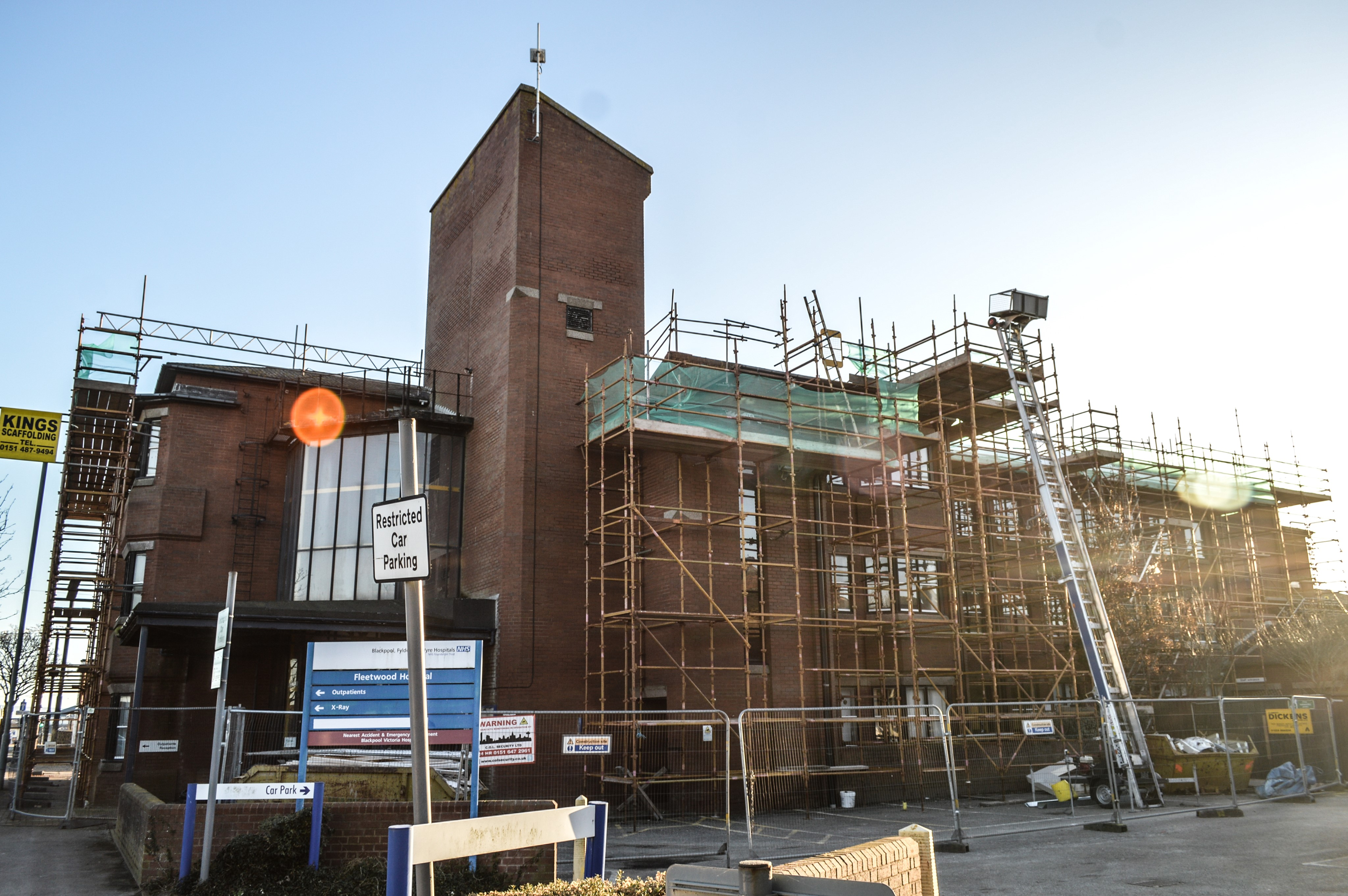 A brick building under renovation with scaffolding and a tall tower. Signs indicate 