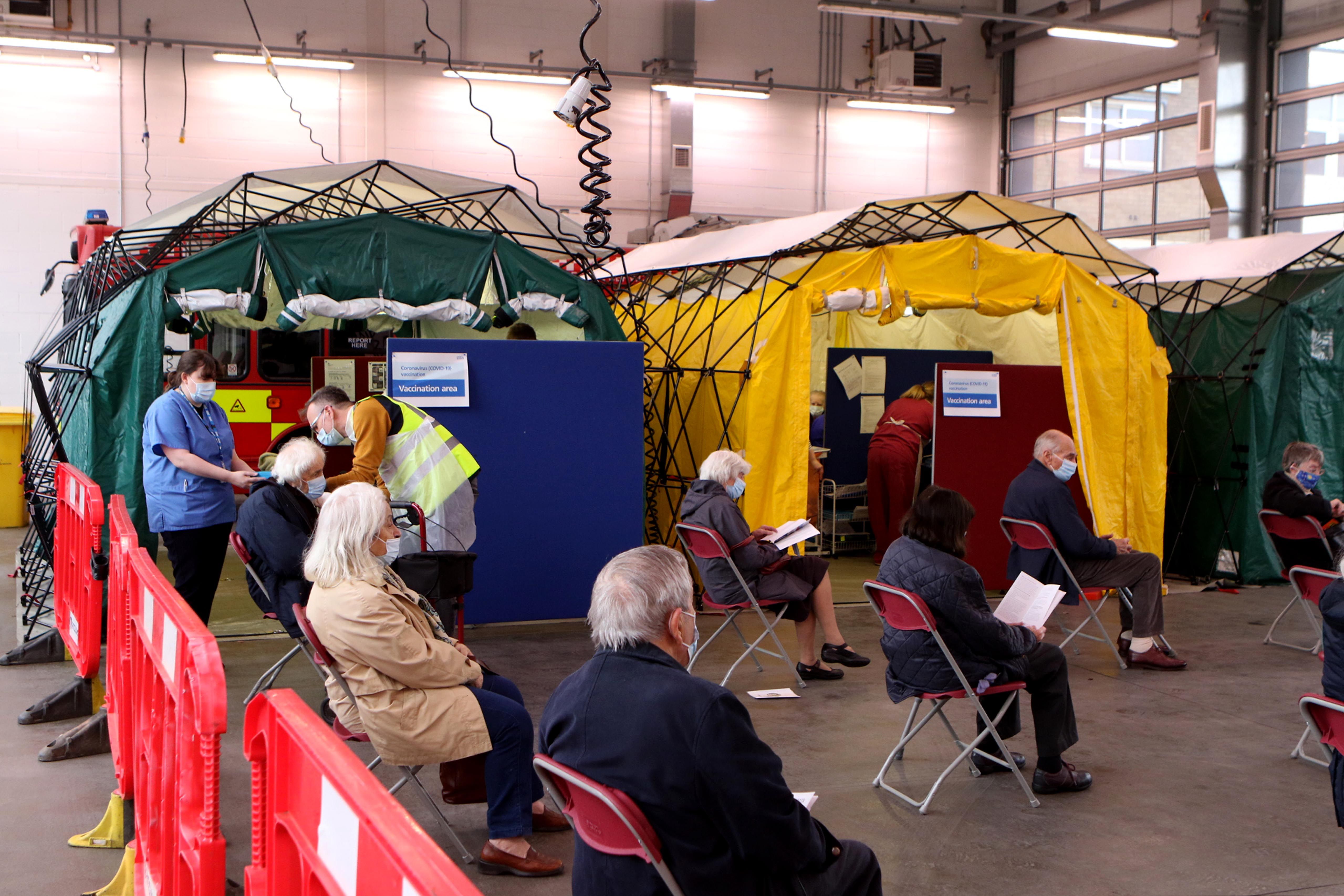 A group of people sit socially distanced awaiting vaccination.