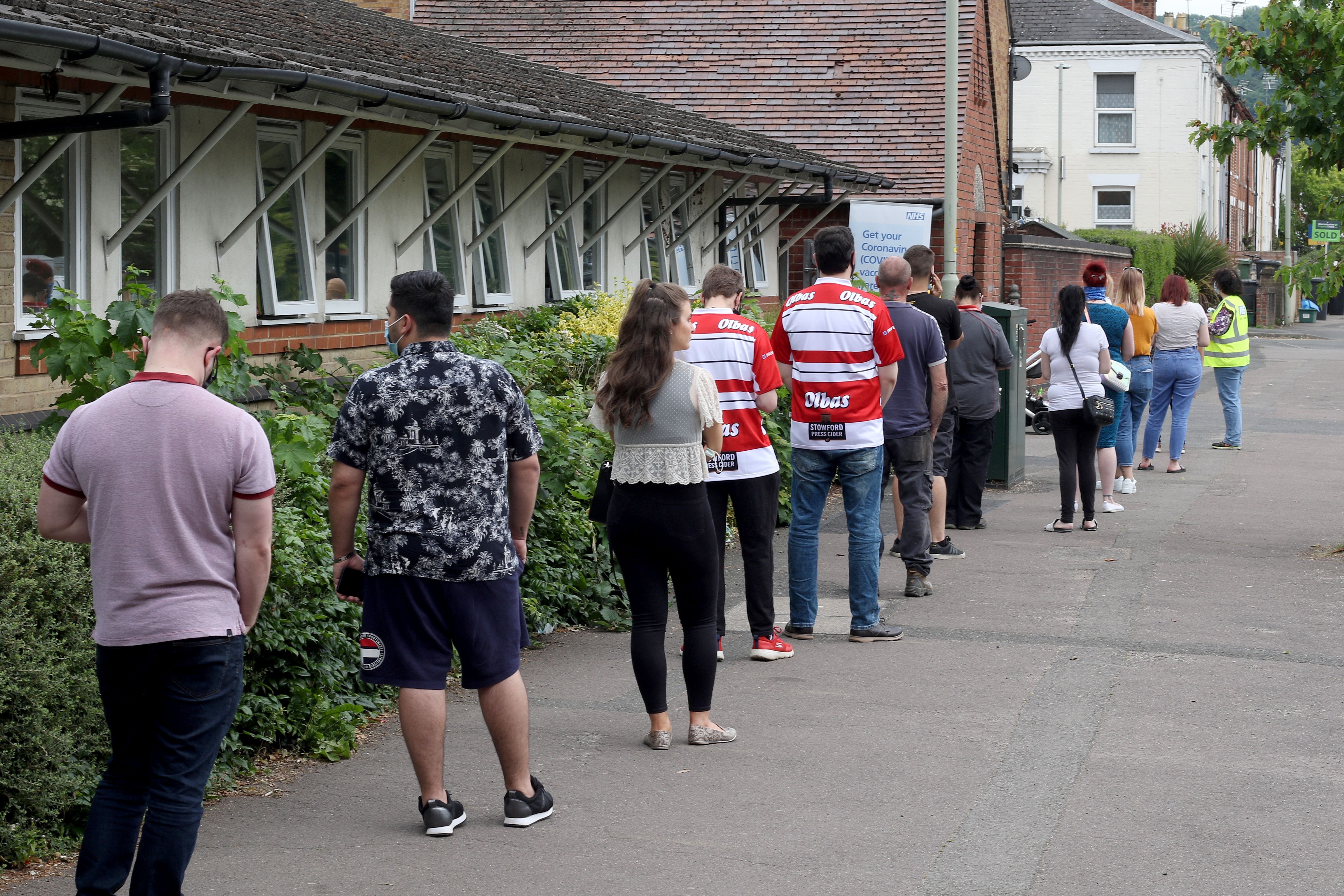 People queuing along a path, socially distanced, waiting outside a clinic for vaccinations.