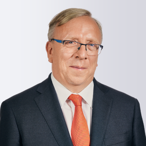 Man in a suit with glasses and an orange tie, looking at the camera with a slight smile, against a light gray background.